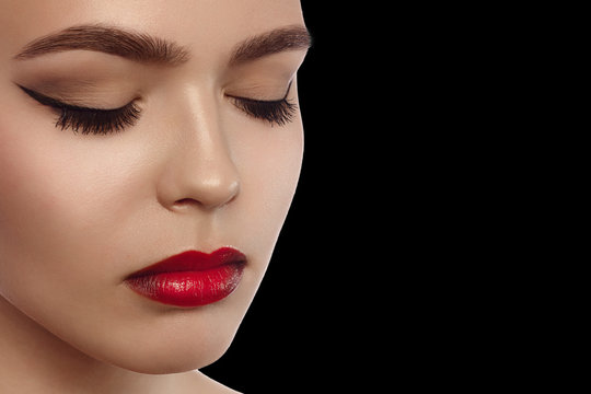 Beauty concept, head and shoulders of woman drawing contour on lips with red lipliner. Portrait of woman touching lips with pencil and looking at camera, studio, black background