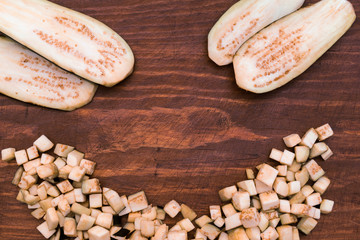 Eggplant, cut into small cubes and wide flat slices on wooden background.