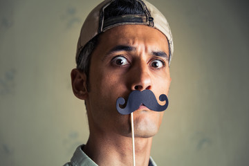 head shot of a man wearing a fake paper mustache looking at the camera