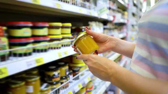 Closeup caucasian woman hand near shop shelves choosing light honey jar in grocery market. female customer checking product ingredients. supermarket, sale, shopping, assortment, consumerism concept