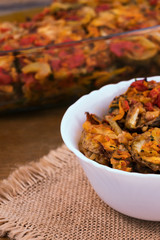 Vegetables, sliced and fried in vegetable oil, in a glass container for frying, one serving in a white bowl, linen napkin on a wooden background, close-up.