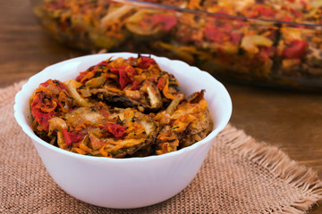 Serving vegetable stew of fried zucchini, tomatoes, onions, carrots and peppers in a white plate on a linen napkin, close-up, wooden background.