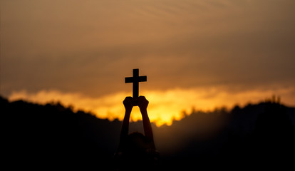 hands holding christian cross with light sunset background. silhouette concept