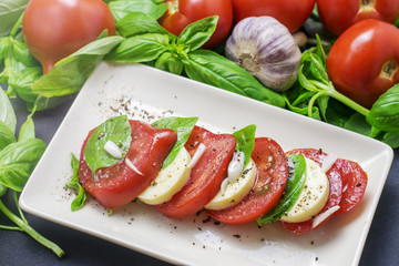 Traditional italian food, sliced tomatoes and mozzarella and basil on a white plate
