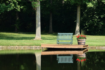 Obraz premium Empty Bench and Geraniums in Barrel Beside Pond for Quiet Reflection