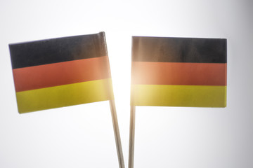 Two mini flags of Germany on white background. Light flare effect on the center of the photo.