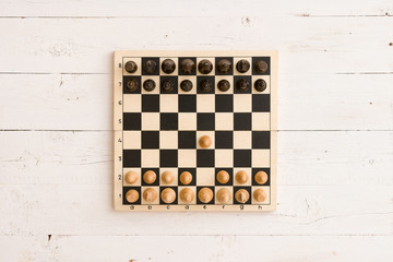 Top view on wooden chess board with figures during the game on white wooden table background. First...