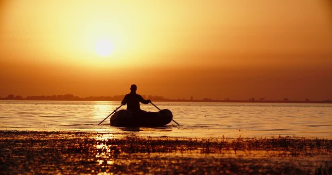 experienced Fisherman rowing with paddles in a rubber boat in a lake in sunset 4k