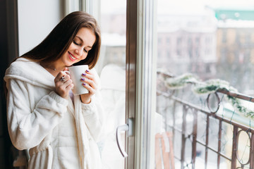Young beautiful smiling woman dreaming standing near the window