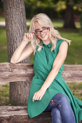 one young woman, 25 years old, sitting in wood bench in park, green dress,  happy positive portrait. holding eyeglasses, smiling.