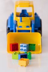 Children toy tractor with colorful plastic bricks on white background. Baby's toys on the table isolated.