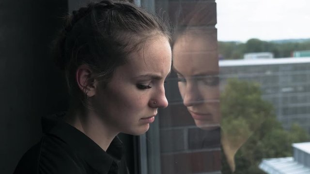 Sad Young Woman Leaning Head Against Glass Window