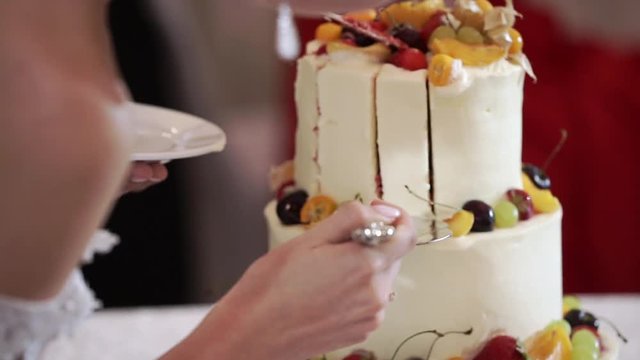 Bride and grrom cutting pieces of white wedding celebration cake with fruits at the party event
