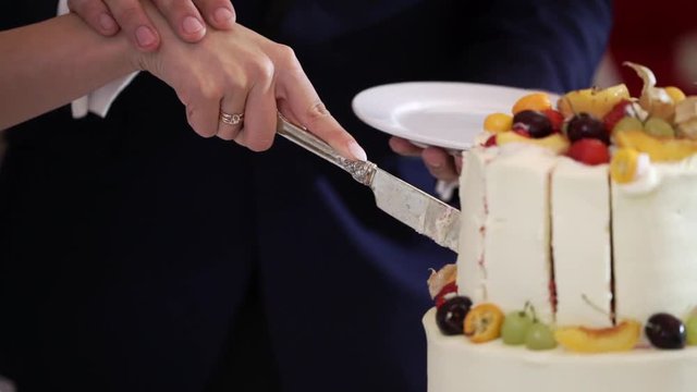 Bride and grrom cutting pieces of white wedding celebration cake with fruits at the party event