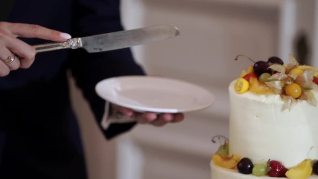 Bride and grrom cutting pieces of white wedding celebration cake with fruits at the party event