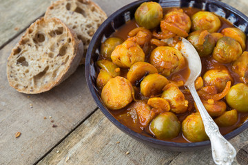 Roasted fresh brussels sprouts in homemade ceramic bowl on natural wooden background.