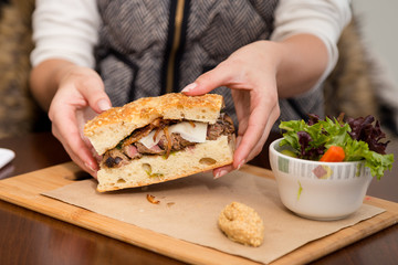 A steak sandwich on focaccia bread with a side salad.