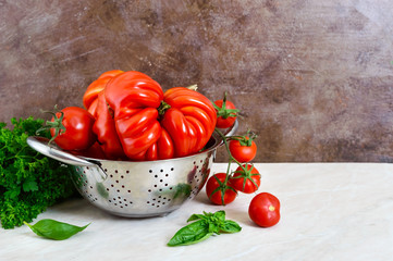 Ripe juicy tomatoes of different varieties, green fragrant basil on the table. Italian Cuisine.