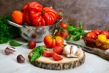 Ripe juicy tomatoes of different varieties, green fragrant basil, garlic on the table. Italian Cuisine.