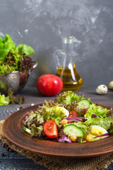 Tasty vegetarian salad with fresh vegetables, herbs, quail eggs, chickpeas in a clay bowl on a wooden table. Proper nutrition. Healthy food.