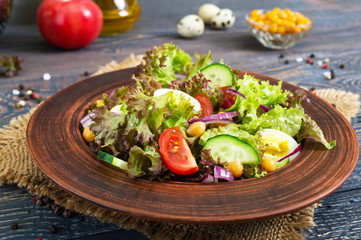 Tasty vegetarian salad with fresh vegetables, herbs, quail eggs, chickpeas in a clay bowl on a wooden table. Proper nutrition. Healthy food.