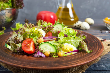 Tasty vegetarian salad with fresh vegetables, herbs, quail eggs, chickpeas in a clay bowl on a wooden table. Proper nutrition. Healthy food.