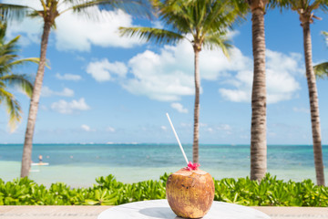 Fresh coconut on a white table beside a tropical beach with palm trees.