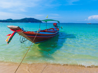 One colorful Thai Longtail boat with ribbons, anchored at a beach on a bright sunny day, with calm waters and bright blue skies and islands in the background. Shot on Ko Pha Ngan, Thailand.