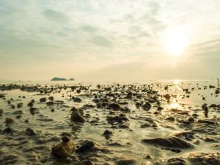 Beautiful beach sunset on a cloudy day at low tide, with islands on the horizon and the blue and orange sky reflecting in the water on the beach. With stones, shells and seaweed in the foreground.