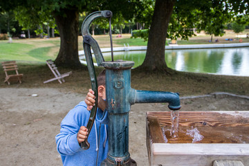 Junge an manueller Schwengelpumpe pumpt Wasser