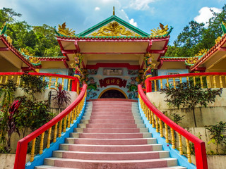 Stairs leading to the Goddess of Mercy Temple Shrine in Chaloklum, Ko Pha Ngan, with trees and cloudy skies in the background.