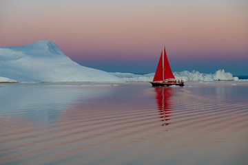 Greenland after midnight glow light iceberg mirror panorama with red sail ship 