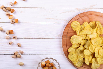 Snacks on a white wooden table. Chips, pistachios, dry cheese.
