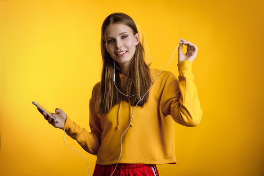 beautiful girl listening to music on headphones, photo in studio on yellow background