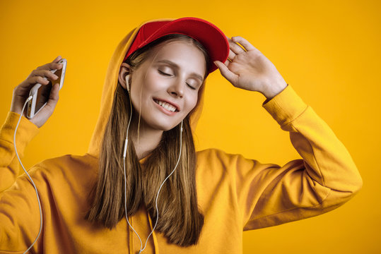 beautiful girl listening to music on headphones, photo in studio on yellow background