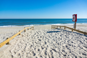 Beach entrance next to Lifebuoy. White sand and blue clear water.