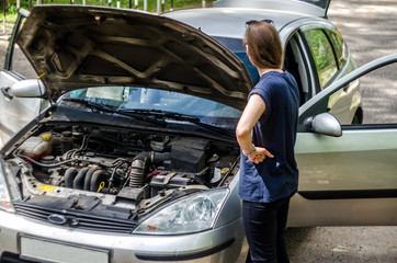 Girl driver near the open hood of a broken car. Broken car on the roadside with an open hood, trunk and doors.