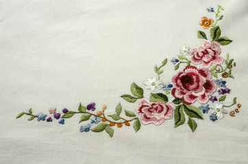 Embroidered corner with a bouquet of pink- red roses with small multicolored flowers and bright berries on white cotton fabric