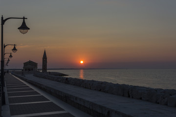 Silhouette of the church with tower and series of lamps during sunrise over the sea on the stone beach.