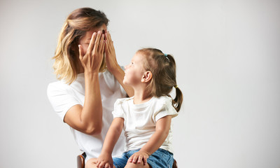 Little girl playing peekaboo game with her mother on white background with copy space. Woman and...
