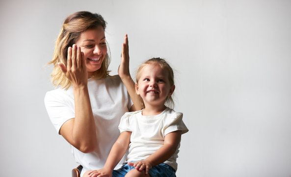 Little girl playing peekaboo game with her mother on white background with copy space. Woman and child are playing peek-a-boo and having fun. Parenthood and happy moments concept