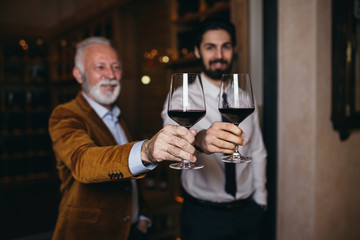 Winemakers in wine cellar holding glass of wine and checking it. Sommeliers testing wines in winery.