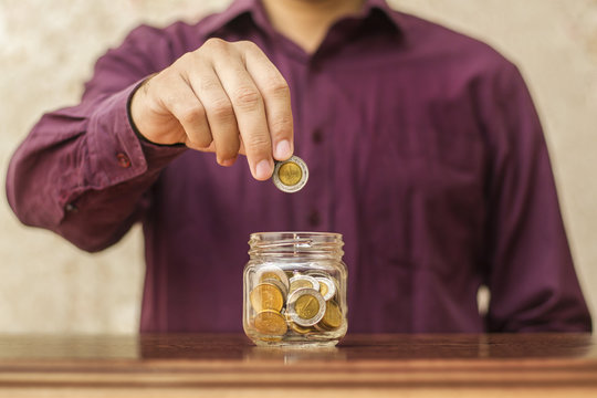 Youngman Putting Coin in Glass Jar Full of Coins, Saving Concept, Egyptian Pounds