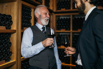 Winemakers in wine cellar holding glass of red wine and talking.