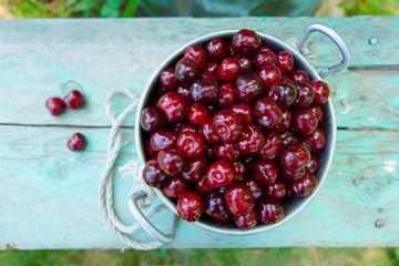 An old tin pan filled with ripped red cherries. A pot of ripped cherries in the garden. Freshly picked and washed berries stand on an old bench of beautiful turquoise color in the garden. Top view.