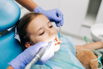 Cute little girl sitting on dental chair and having dental treatment.