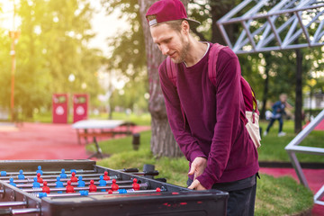 smiling young man playing table soccer foosball outside having fun with friends