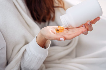 Vitamins and food supplements concept. Closeup of female hand pouring yellow pills out of bottle into palm. Woman spilling out medication, tablets, capsules on hand.