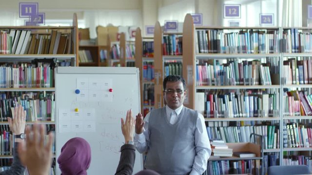 Tilt down of cheerful middle eastern male teacher in eyeglasses smiling and answering questions of migrant students during English lesson