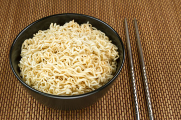 Instant noodles in a black bowl on Japanese mat and chopsticks